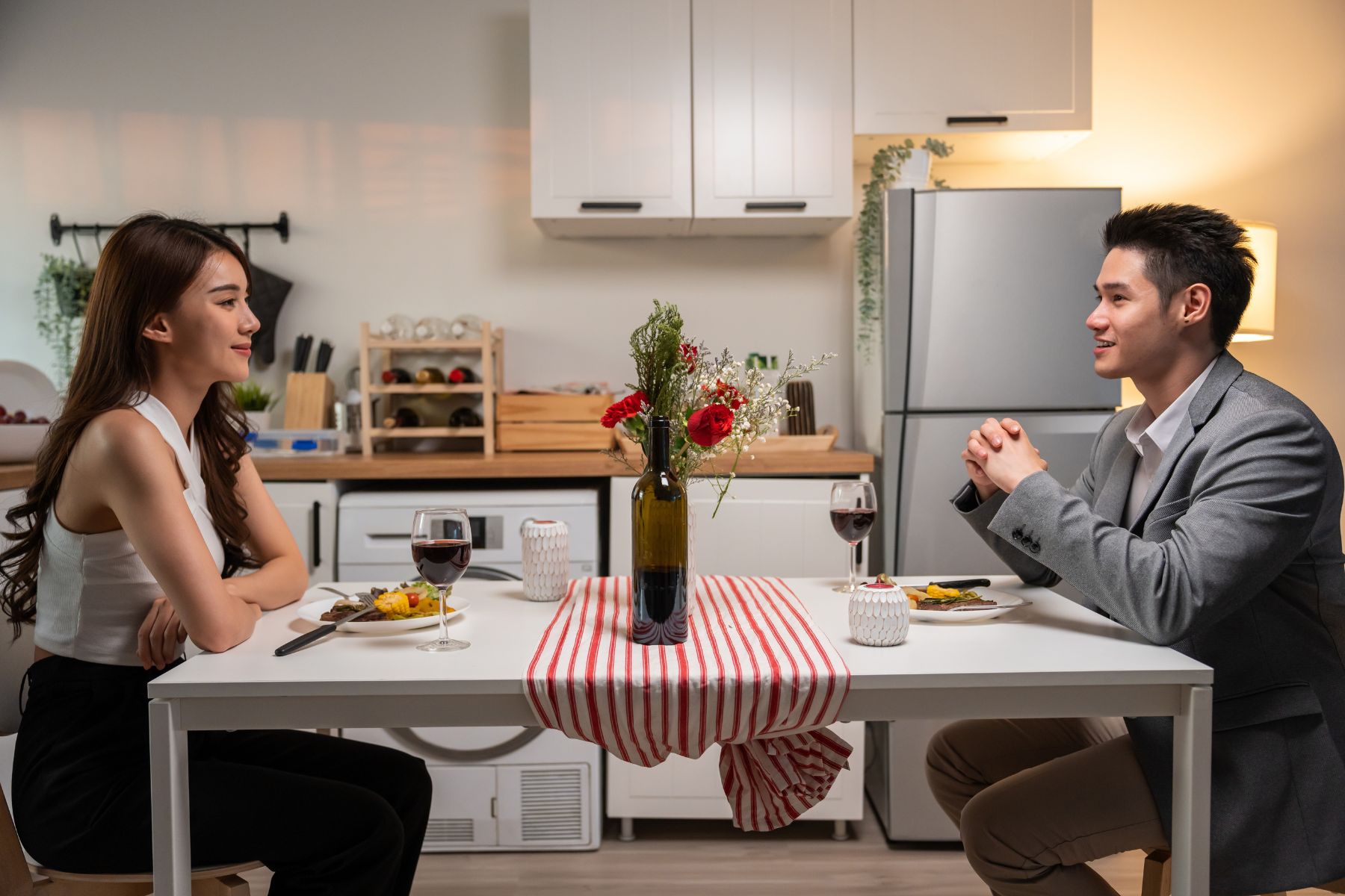 Asian young couple having dinner to celebrate valentine's day together. Attractive romantic new marriage man and woman having night party eat foods on table for wedding anniversary in kitchen at home.