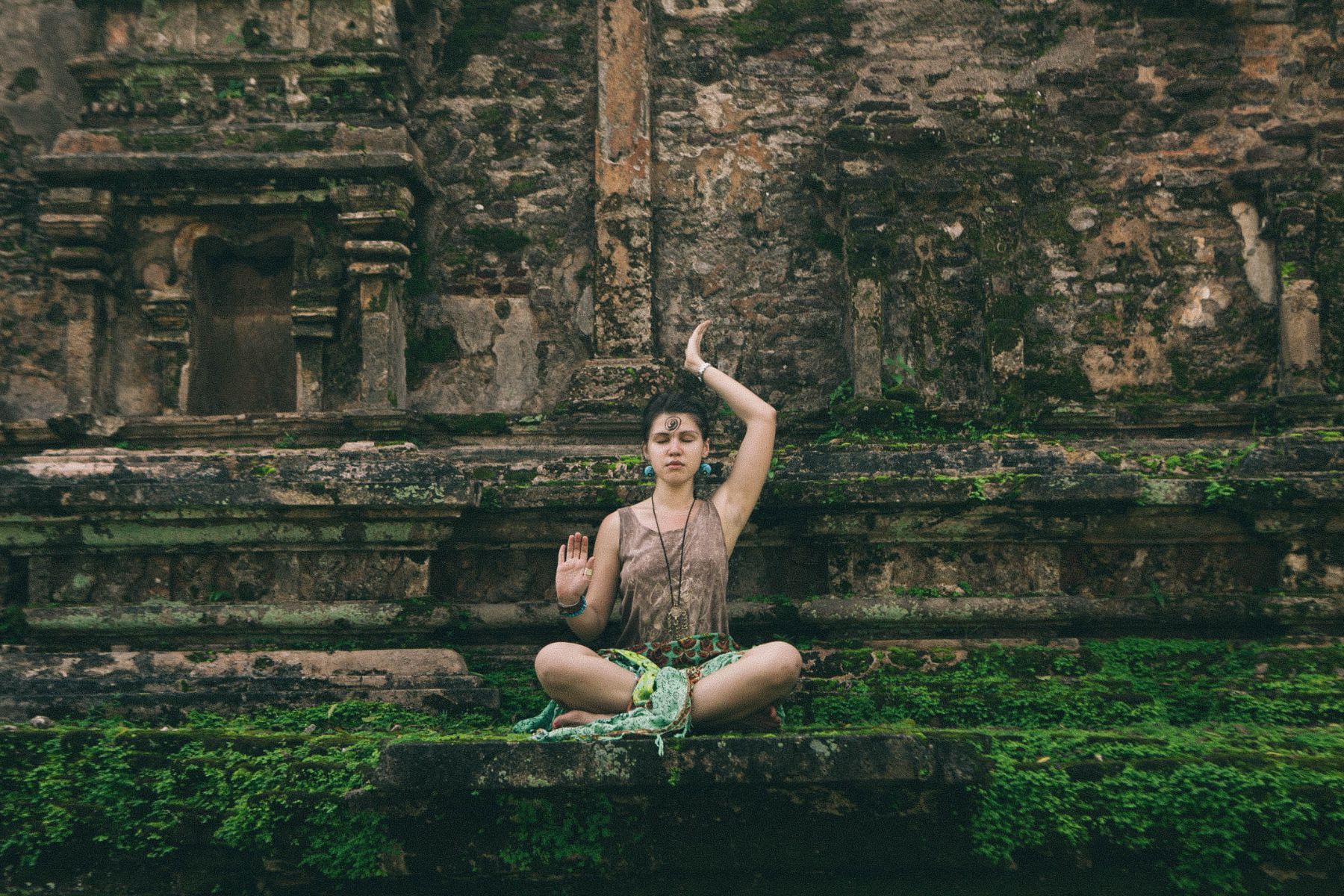 the girl sits in a lotus pose and meditates against the background of the ancient temple on Sri Lanka
